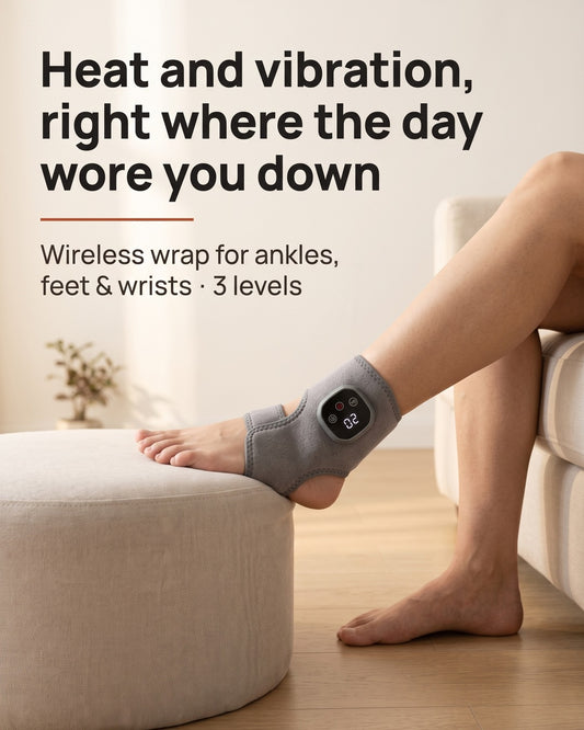 Gray wireless heat and vibration wrap worn on an ankle, foot resting on an ottoman.